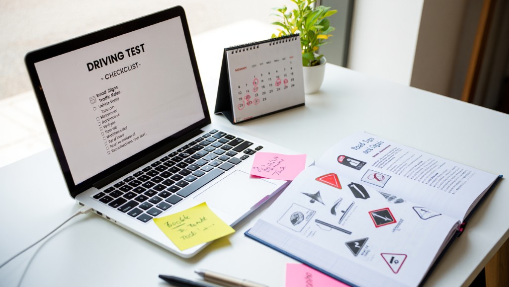 Desk with laptop driving test checklist, road signs textbook, and calendar — plan theory and awareness